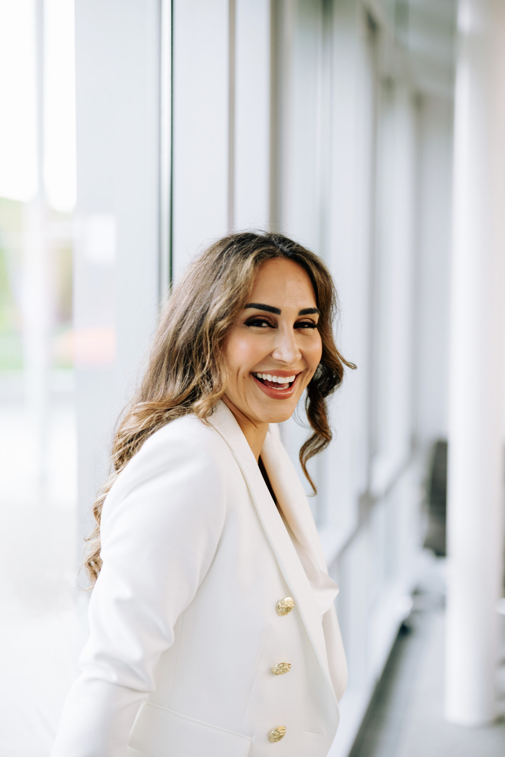 woman smiling confidently in a white blazer with gold buttons during a modern brand photoshoot at Newport Civic Center, captured by Dana Gaydon